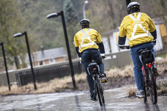 Photo of two volunteers in yellow jackets riding bikes on bike patrol.