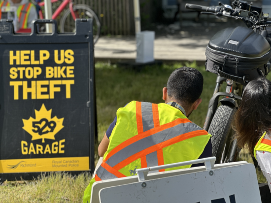 Bénévole avec un gilet de sécurité qui procède à l’inspection d’un vélo. Le panneau au sol indique « Aidez-nous à lutter contre les vols de vélos. 529 Garage. »