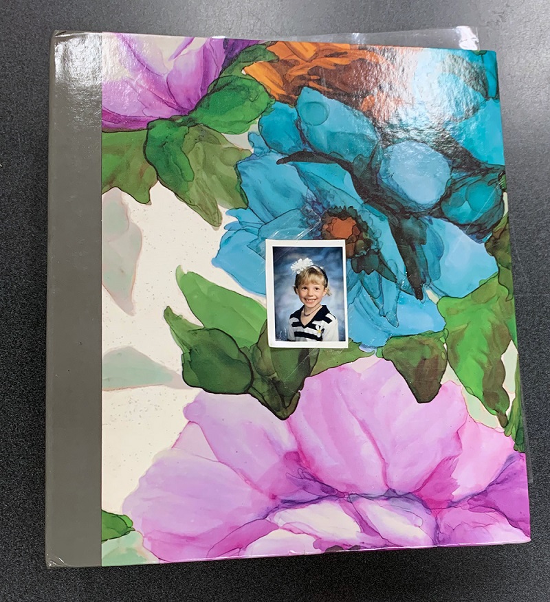 Photo album with multi-coloured flowers and a school picture of a little girl taped on the front