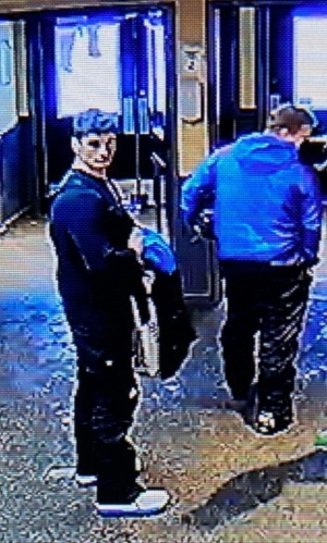 Les deux suspects se tiennent debout ensemble dans une entrée de porte. L’un d’entre eux est entièrement vêtu de noir et l’autre porte une veste bleue. 