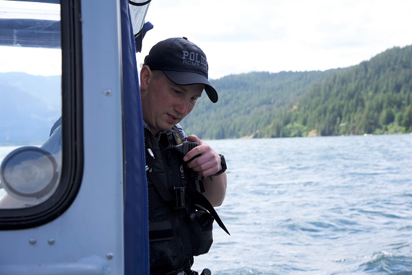 Le gendarme Kyle Toole parle dans le radiotéléphone portatif de la police pendant qu’il est à la barre de l’embarcation Zodiac de la GRC en Colombie Britannique, sur le lac Harrison.