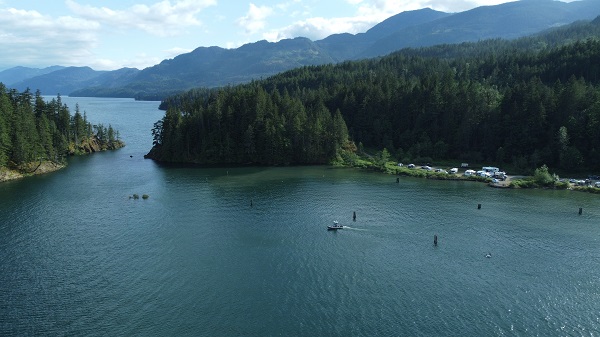 Une photographie aérienne de l’embarcation Zodiac de la GRC en Colombie Britannique sur le lac Harrison, au site de camping Ten Mile Bay. Des campeurs se trouvent à l’intérieur de véhicules et de remorques garés au bord de l’eau.