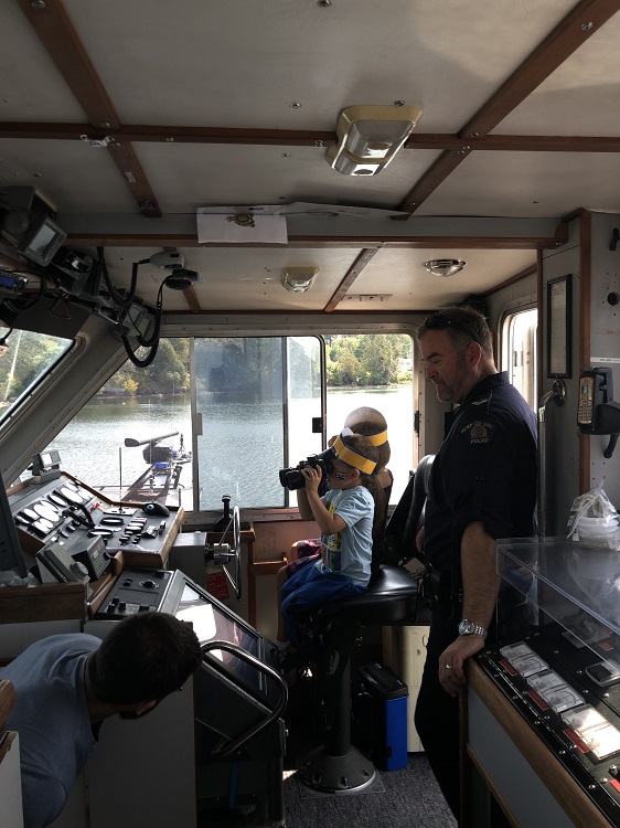 •&#9;Un agent de la GRC et un jeune garçon se trouvent sur la passerelle d’un bateau de police. Le garçon porte une casquette semblable à une casquette de police et regarde dans des jumelles. 