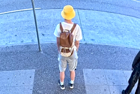 Photo of Ryan Liu standing on the street, wearing beige shorts, a white t-shirt, black shoes, yellow hat and brown backpack